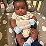 Tyler joined the competition — help win amazing prizes! baby, infant, child, curly_hair, mittens, socks, onesie, cushion, cloud_pattern, gray, beige, indoor, crib, person, cute, plush, seated, looking, portrait, soft_lighting