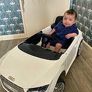 Ismael participe au concours pour gagner de l'argent avec cette photo : baby, child, toy_car, audi, indoor, flooring, wallpaper, blue_clothing, sitting, steering_wheel, curious_expression, small_wheels, floor, car_toy, person, head, face, seat, vehicle, play