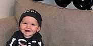George is registered to the contest to win money with this photo: baby, child, smiling, skeleton_costume, hat, balloons, boo, couch, grey_couch, indoor, happy, festive, halloween, costume, cute, feet, hands, face, infant, portrait