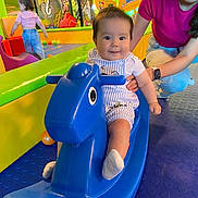 Amilia a rejoint le concours — aidez-le/la à gagner de superbes lots ! adult, baby, blue, child, clothing, colorful, floor, fun, happy, indoor, person, pink, play, play_area, playground, rocking_horse, smile, supporting_hand, toddler, toy