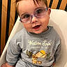 baby, child, glasses, smile, blue_clothing, sitting, chair, wooden_background, cute, portrait, indoor, toddler, happy, face, casual_wear, long_sleeves, cactus_print, cartoon, cozy, hair