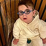 Demir participe au concours pour gagner de l'argent avec cette photo : toddler, child, glasses, blue_glasses, sitting, hoodie, cream_clothing, transparent_chair, wooden_background, indoor, expression, curious, person, baby, face, head, hand, feet, casual_wear, young_child