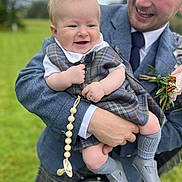 Archie joined the competition — help win amazing prizes! accessory, baby, celebration, child, clothing, family, footwear, grass, happy, holding, man, nature, outdoor, pacifier, person, plaid, portrait, smile, suit, tie