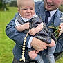 accessory, baby, celebration, child, clothing, family, footwear, grass, happy, holding, man, nature, outdoor, pacifier, person, plaid, portrait, smile, suit, tie