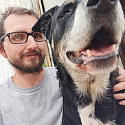 Flynn Rider is registered to the contest to win money with this photo: background, beard, black_and_white_dog, casual, closeup, dog, face, friendly, glasses, hand, happy, indoor, light_gray_shirt, man, pet, portrait, selfie, smile, tongue_out, window