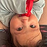 baby, child, infant, portrait, upside_down, smiling, eyes, face, red_toy, toy, hands, long_sleeves, clothing, dark_hair, lying_down, indoor, close_up, playful, cozy, photography