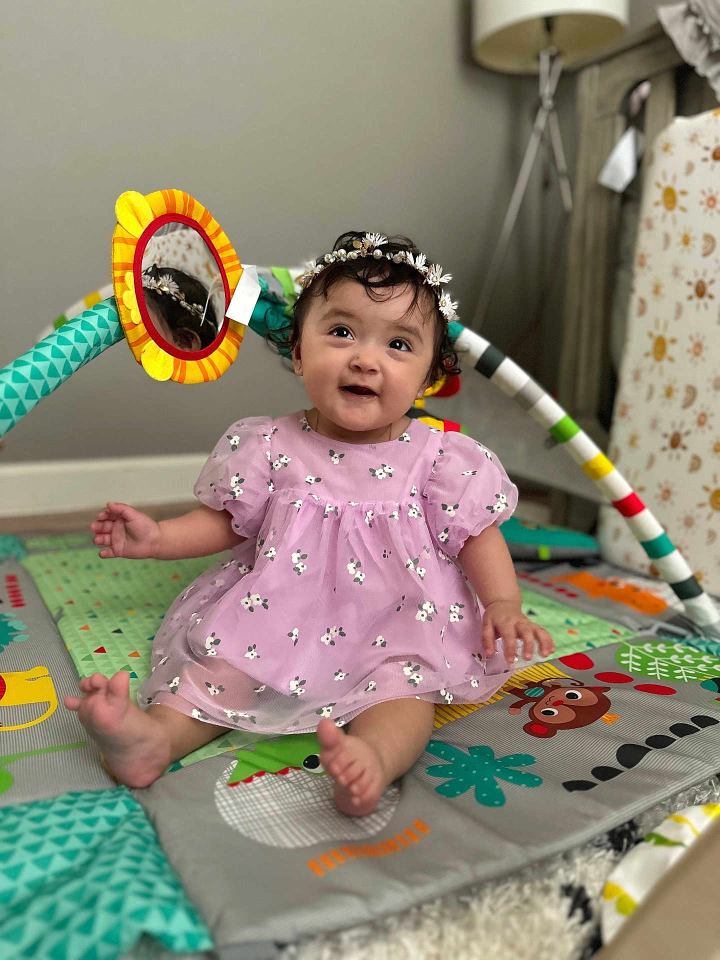 Romina is registered to the contest to win money with this photo: baby, child, girl, purple_dress, floral, headband, daisy, play_mat, mirror_toy, colorful, sitting, smiling, indoor, lamp, curly_hair, cute, happy, toys, floor, portrait