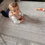 Lucas a rejoint le concours — aidez-le/la à gagner de superbes lots ! baby, child, curious, lying_down, rug, patterned_rug, toy, crib, indoor, floor, clothing, vest, long_sleeve, pants, sock, person, infant, looking_up, home, flooring