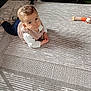 baby, child, curious, lying_down, rug, patterned_rug, toy, crib, indoor, floor, clothing, vest, long_sleeve, pants, sock, person, infant, looking_up, home, flooring