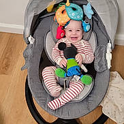 Shifra is registered to the contest to win money with this photo: baby, baby_rocker, striped_pajamas, mickey_mouse_toy, plush_toy, hanging_toys, indoor, wooden_floor, blanket, baby_items, toy_phone, smiling, child, seat, happy, infant, floor, playful, cute, cozy