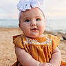 baby, child, blue_eyes, headband, bow, dress, mustard_yellow, embroidery, sand, beach, outdoor, portrait, cute, smiling, infant, hands, sunset, nature, person, fashion