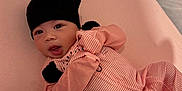 Heaven is registered to the contest to win money with this photo: baby, infant, pink, black_hat, pajamas, striped_clothing, lying_down, soft_surface, cute, child, newborn, indoors, person, face, hand, sleeping_area, cozy, expression, looking_at_camera, comfortable