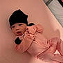baby, infant, pink, black_hat, pajamas, striped_clothing, lying_down, soft_surface, cute, child, newborn, indoors, person, face, hand, sleeping_area, cozy, expression, looking_at_camera, comfortable