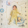 baby, infant, child, portrait, lying_down, smiling, face, onesie, yellow_clothing, teddy_bear, blanket, moon, clouds, stars, nursery, milestone, monthly_photo, indoor, top_down_view, cute