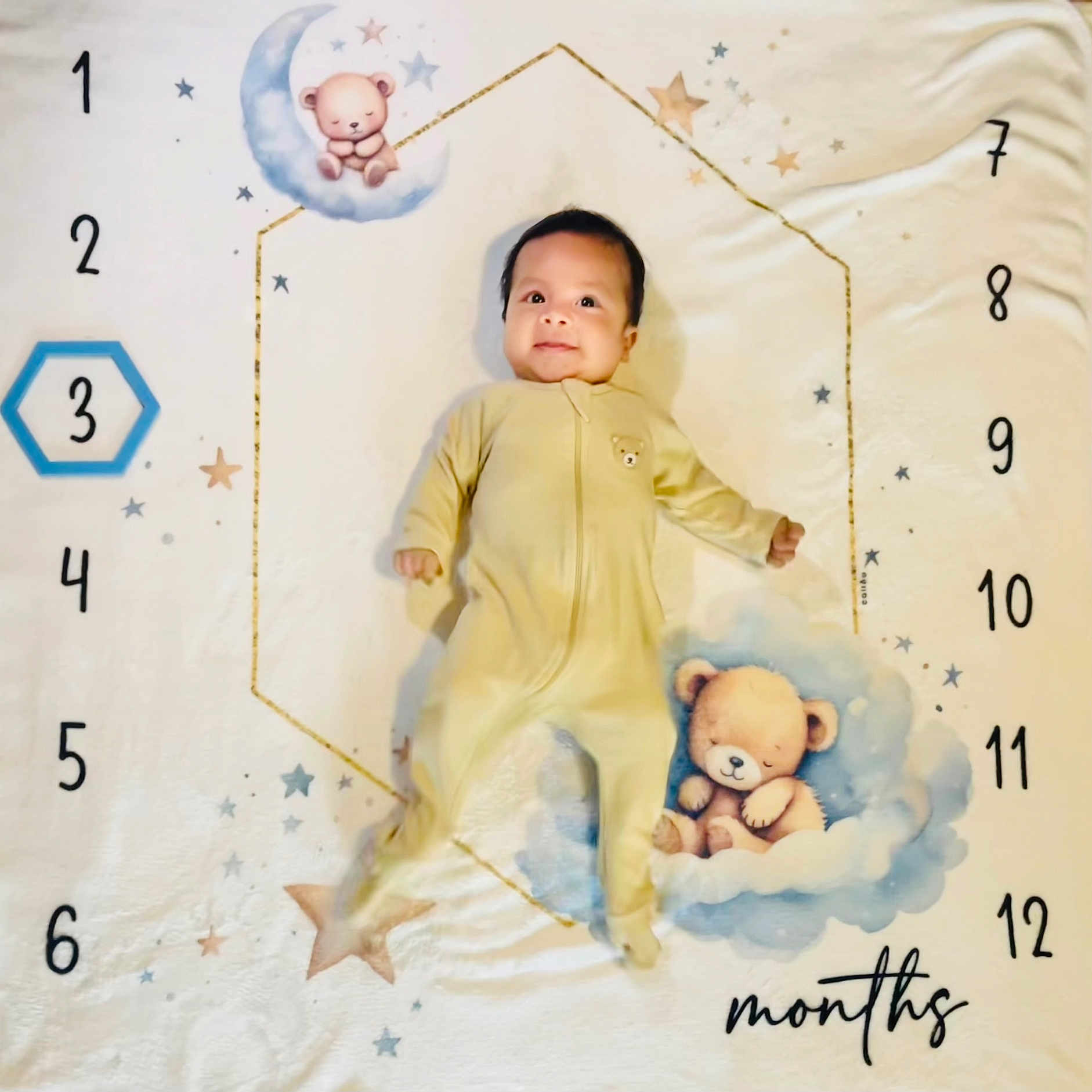 Jorge is registered to the contest to win money with this photo: baby, infant, child, portrait, lying_down, smiling, face, onesie, yellow_clothing, teddy_bear, blanket, moon, clouds, stars, nursery, milestone, monthly_photo, indoor, top_down_view, cute