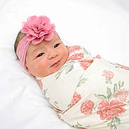 Gia joined the competition — help win amazing prizes! baby, newborn, infant, swaddled, headband, flower, pink, floral_blanket, cute, portrait, sleeping_area, soft_lighting, white_background, child, face, smile, human, cozy, wrapped, adorable