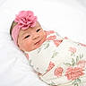 baby, newborn, infant, swaddled, headband, flower, pink, floral_blanket, cute, portrait, sleeping_area, soft_lighting, white_background, child, face, smile, human, cozy, wrapped, adorable