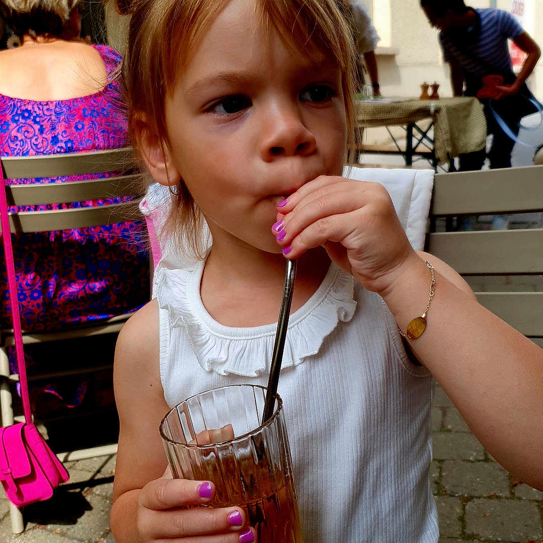 Thylia participe au concours pour gagner de l'argent avec cette photo : bracelet, building, casual, chair, child, daylight, drinking, glass, nail_polish, outdoor, pavement, people, person, portrait, relaxed, side_view, straw, table, white_clothing, window
