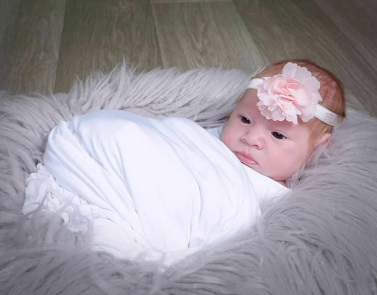 Scarlett joined the competition — help win amazing prizes! baby, infant, blanket, headband, flower, pink, cushion, fluffy, soft, face, wrapped, lying_down, newborn, portrait, indoors, floor, cozy, cute, calm, child