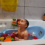 Charlie a rejoint le concours — aidez-le/la à gagner de superbes lots ! baby, bath_time, bathroom, bathtub, blue_tub, child, child_playing, cute, fun, indoor, infant, looking_up, plastic_toys, sitting, smiling, tiled_wall, toys, water, wet_hair, yellow_bag