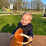 Léon participe au concours pour gagner de l'argent avec cette photo : child, toddler, playground, playground_equipment, rocker, smile, outdoor, grass, trees, park, daylight, person, clothing, jacket, pants, happy, sunlight, shadow, recreation, leisure