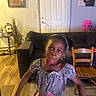 child, girl, living_room, couch, chair, floor, door, painting, wooden_floor, decor, playful, motion_blur, tongue_out, short_sleeve, pink_pants, home, furniture, person, indoor, happy