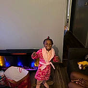 Grace joined the competition — help win amazing prizes! child, girl, smiling, robe, pink, slippers, living_room, electric_fireplace, gift_bag, toy, wood_floor, wall, doorway, furniture, person, happy, indoor, home, celebration, cozy