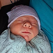 Zakiyah joined the competition — help win amazing prizes! newborn, baby, sleeping, swaddled, blanket, hat, person, tattoo, teal_shirt, closeup, face, infant, peaceful, resting, cozy, indoor, skin, portrait, child, human