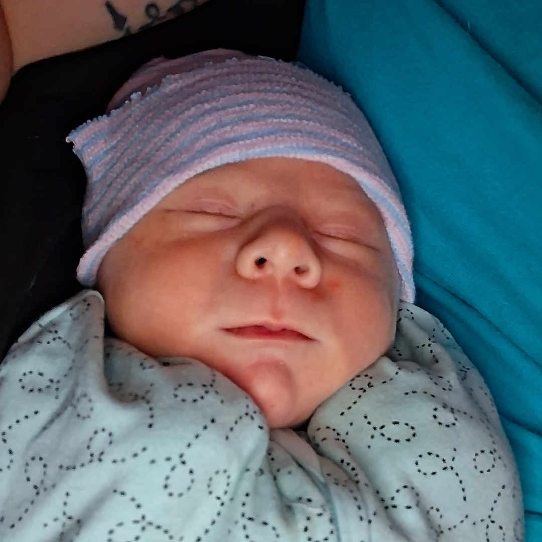 Zakiyah joined the competition — help win amazing prizes! newborn, baby, sleeping, swaddled, blanket, hat, person, tattoo, teal_shirt, closeup, face, infant, peaceful, resting, cozy, indoor, skin, portrait, child, human