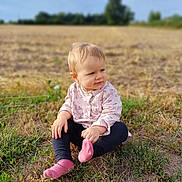 Thalia a rejoint le concours — aidez-le/la à gagner de superbes lots ! toddler, child, grass, field, outdoor, nature, pink_socks, pink_top, curious, sitting, baby, portrait, daylight, casual_clothing, nature_background, young_child, blond_hair, looking_away, soft_light, rural
