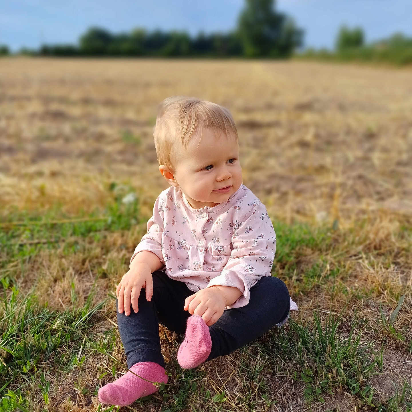 Thalia a rejoint le concours — aidez-le/la à gagner de superbes lots ! baby, blond_hair, casual_clothing, child, curious, daylight, field, grass, looking_away, nature, nature_background, outdoor, pink_socks, pink_top, portrait, rural, sitting, soft_light, toddler, young_child