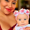 Athena joined the competition — help win amazing prizes! baby, infant, parent, woman, portrait, smiling, flower_crown, headband, close_up, indoor, warm_lighting, red_clothing, baby_clothing, holding, cuddle, family, blue_eyes, face, photography, adorable