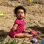 toddler, child, sand, beach, shovel, toy, play, outdoor, grass, water, person, summer, sunlight, sitting, curly_hair, pink_clothing, barefoot, sandcastle, playtime, nature