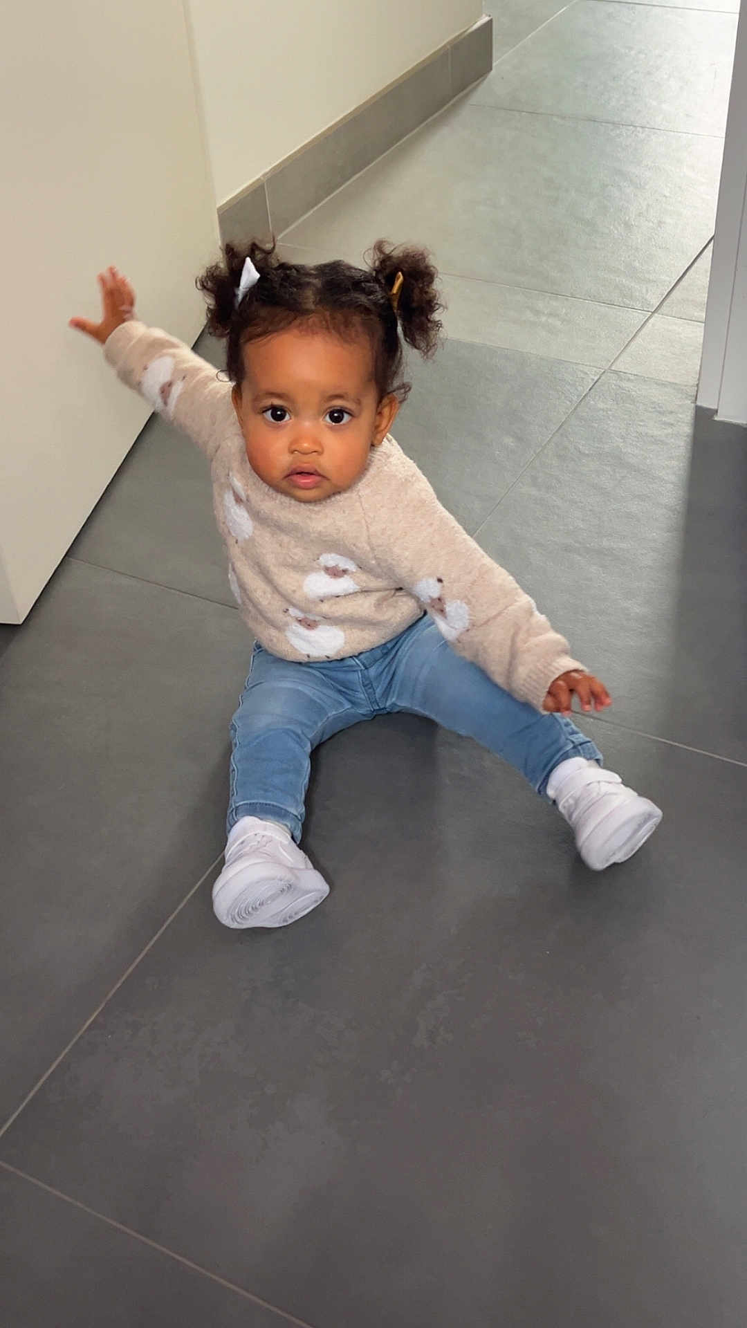 Lila participe au concours pour gagner de l'argent avec cette photo : toddler, child, indoor, floor, tile_floor, sweater, jeans, white_shoes, hair_tied, cute, balancing, sitting, young_child, casual_clothing, portrait, person, baby, expression, candid, home