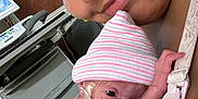 Grayson is registered to the contest to win money with this photo: newborn, baby, infant, hospital, medical_equipment, nasal_cannula, striped_hat, blanket, footprints, person, smiling, closeup, face, care, love, mother, cradling, tenderness, indoor, healthcare