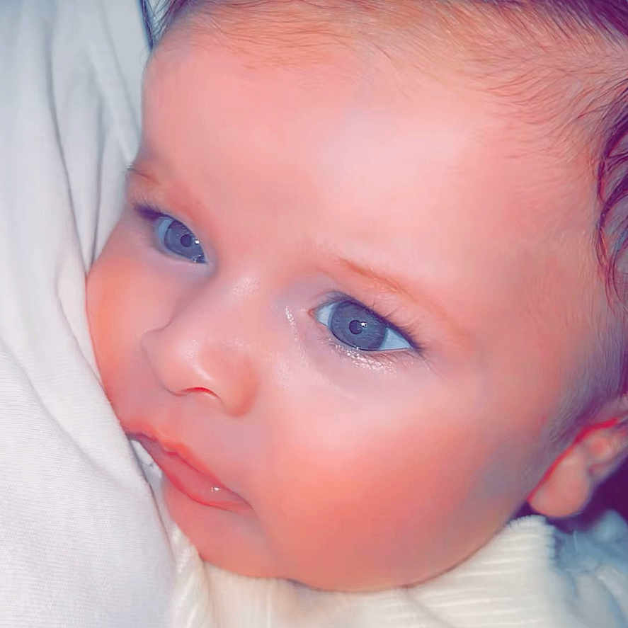 Damiano participe au concours pour gagner de l'argent avec cette photo : baby, face, blue_eyes, curly_hair, close_up, infant, skin, expression, soft_light, white_clothing, portrait, cute, child, small, head, person, indoors, newborn, snuggle, young