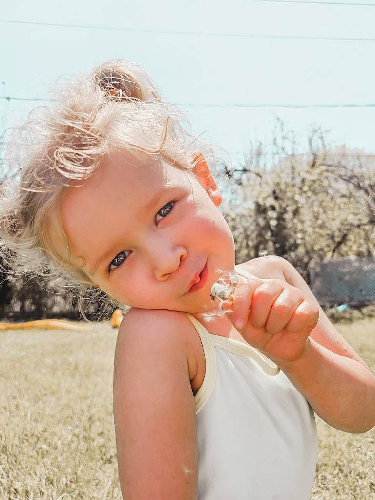 Charlotte is registered to the contest to win money with this photo: blond, brown_hair, child, eye, fashion_accessory, flash_photography, fun, gesture, grass, happy, head, headpiece, lip, people_in_nature, person, sand, skin, sky, smile, toddler