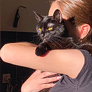 Yumi a rejoint le concours — aidez-le/la à gagner de superbes lots ! black_cat, cat, pet, person, arm, yellow_eyes, indoor, sunlight, holding, animal, feline, close_up, portrait, skin, hair, earring, shadow, tshirt, hand, cozy