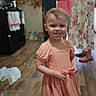 toddler, child, smile, peach_dress, floor, wooden_floor, indoor, kitchen, person, woman, adult, floral_dress, shoes, happy, portrait, family, home, background_blur, standing, candid