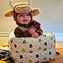 Oliver is registered to the contest to win money with this photo: animal_hat, baby, baby_seat, bull, child, costume, cozy, curious, cute, frog_pattern, hands, indoor, infant, plush, portrait, smiling, soft_texture, warm_lighting, wooden_table, young