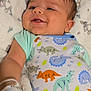 baby, infant, smiling, dinosaur_onesie, clothing, blanket, lying_down, happy, cute, drool, child, portrait, soft_texture, indoor, toddler, face, head, skin, arm, babywear