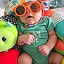 Oliver joined the competition — help win amazing prizes! baby, sunglasses, hat, dinosaur_pattern, onesie, infant, plush_toy, colorful, cushion, indoor, cute, child, smiling, soft_toy, comfort, play_area, clothing, relaxed, portrait, babywear