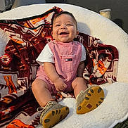 Oliver joined the competition — help win amazing prizes! baby, baby_shoes, blanket, chair, child, clothing, cozy, cute, face, footwear, happy, indoor, infant, patterned_blanket, plush, portrait, romper, sitting, smiling, white_chair