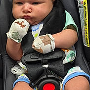 Oliver is registered to the contest to win money with this photo: baby, infant, car_seat, mittens, clothing, straps, red_button, serious_expression, child, cute, seatbelt, closeup, indoor, person, young_child, sitting, head, face, skin, legs