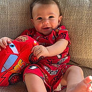 Grayson is registered to the contest to win money with this photo: baby, child, red_clothing, plush_toy, car_toy, smiling, sitting, couch, beige, indoor, happy, cute, infant, sunlight, cozy, portrait, face, foot, hand, texture