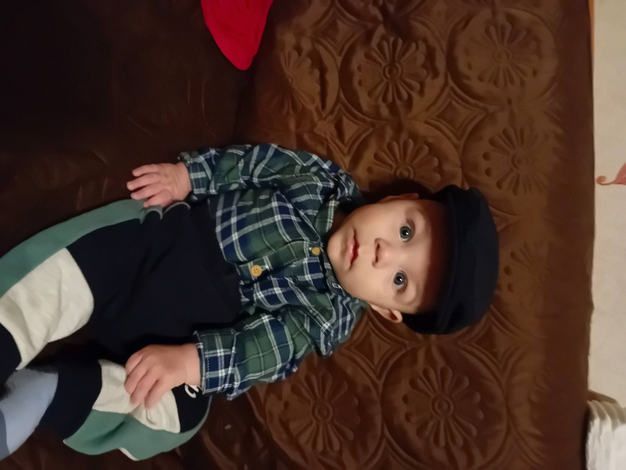 Roberto participe au concours pour gagner de l'argent avec cette photo : baby, baby_toddler_clothing, brown, cheek, child, comfort, elbow, flooring, gesture, hardwood, headwear, human_body, pattern, person, plaid, room, sitting, sleeve, tartan, toddler