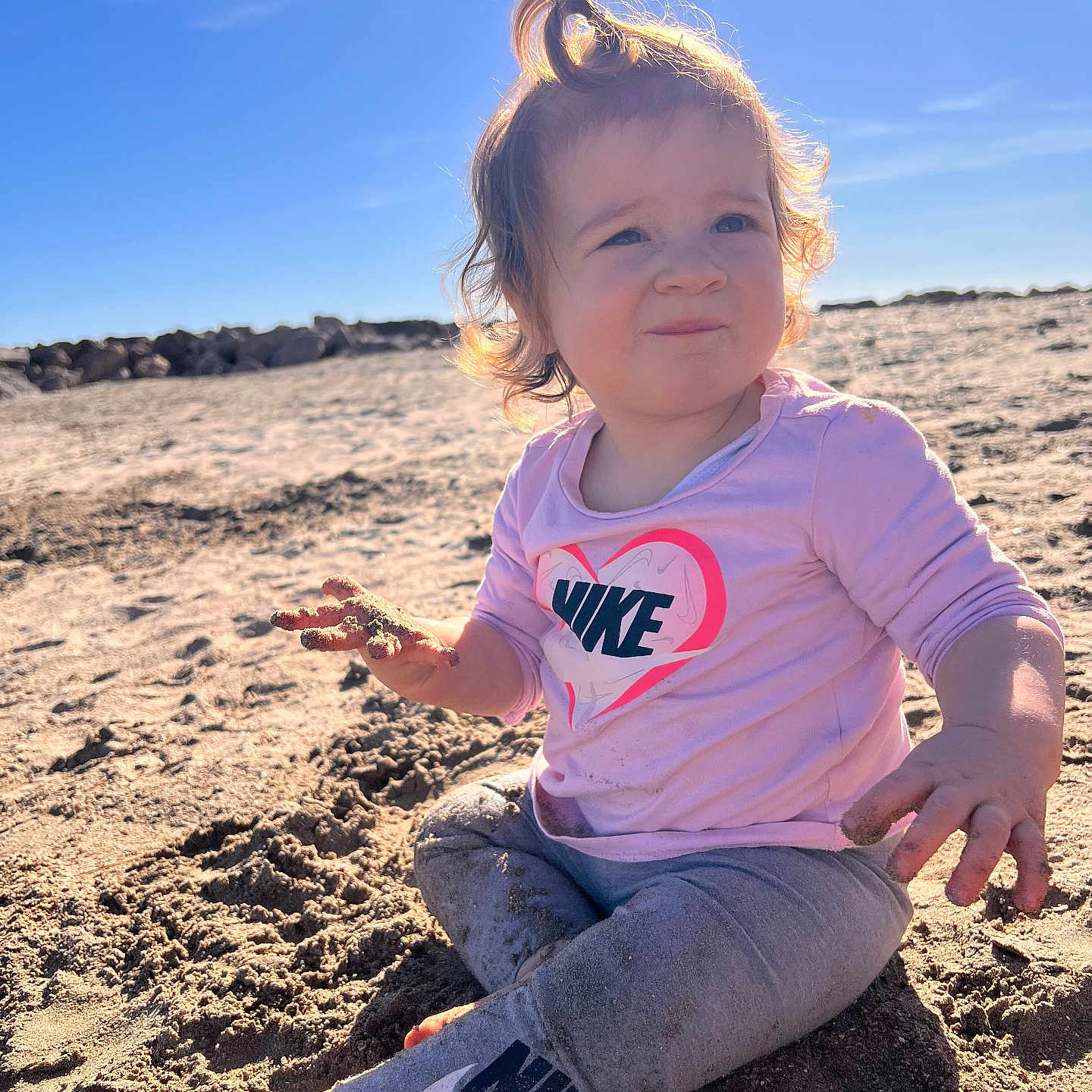 Thaïs participe au concours pour gagner de l'argent avec cette photo : toddler, child, beach, sand, sunlight, curly_hair, pink_shirt, nike_logo, leggings, barefoot, outdoor, daytime, playful, portrait, sitting, casual_clothing, sunny, young_child, nature, curious_expression
