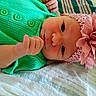 baby, infant, child, portrait, lying_down, green_outfit, pink_hat, flower, headwear, wide_eyes, face, hand, fist, indoors, blanket, textile, closeup, colorful, cute, photography