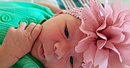 Rylee is registered to the contest to win money with this photo: baby, bed, blanket, child, close_up, colorful, cute, eyes, face, green_outfit, hand, headband, indoor, infant, looking_at_camera, lying_down, photography, pink_flower, portrait, soft_lighting