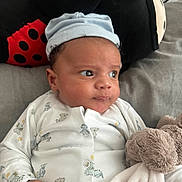Leon is registered to the contest to win money with this photo: baby, infant, plush_toy, cap, onesie, animal_print, pillow, ladybug, bed, blanket, hand, face, eyes, cute, soft_toy, child, indoor, resting, portrait, newborn